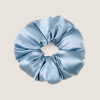 Een extra grote, vergrijsd blauwe scrunchie van moerbeizijde op een zachtbeige achtergrond.