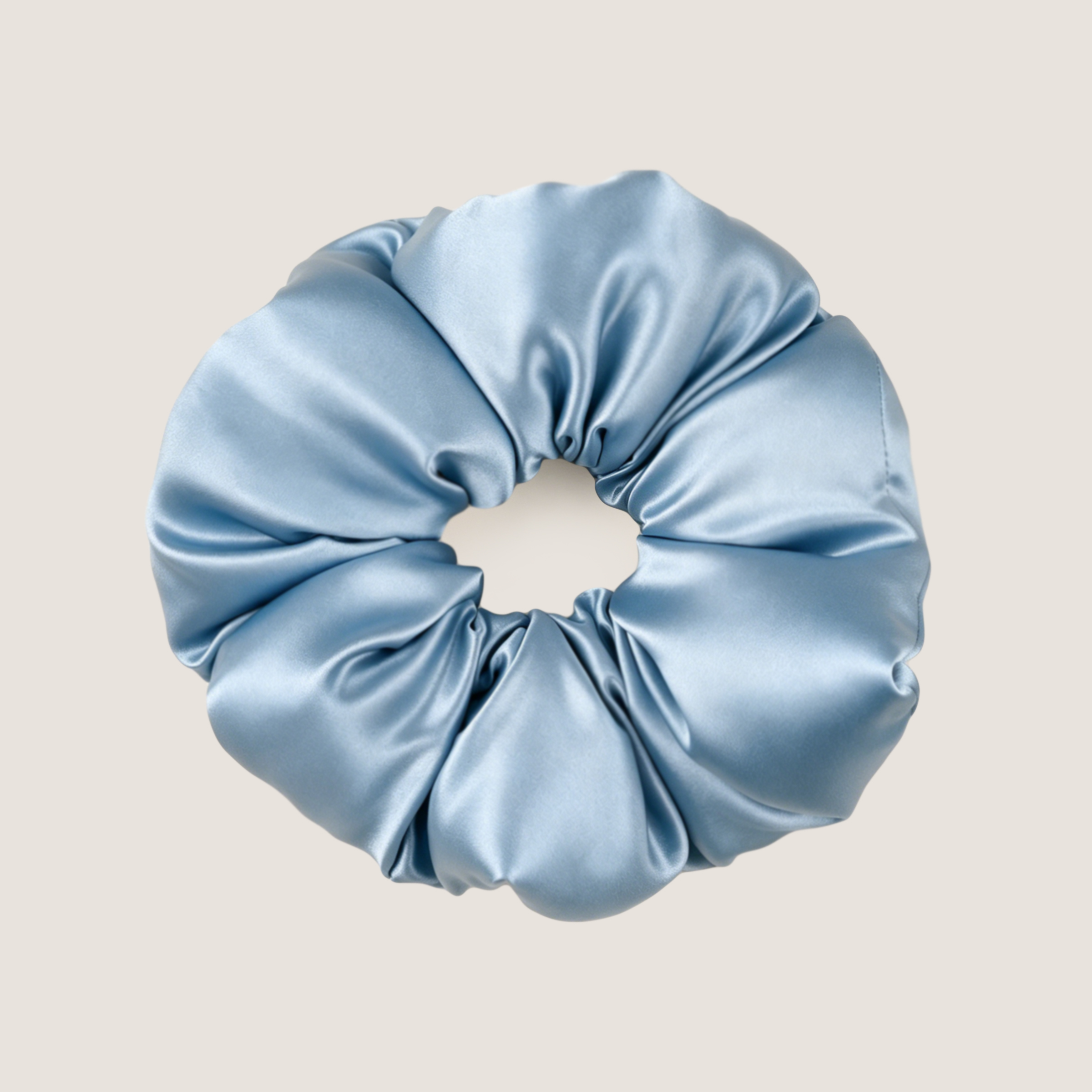 Een extra grote, vergrijsd blauwe scrunchie van moerbeizijde op een zachtbeige achtergrond.