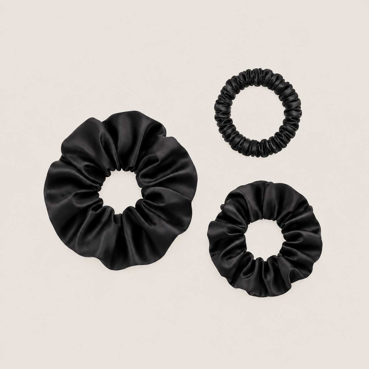 Set van zwarte scrunchies van moerbeizijde in drie maten op een neutrale achtergrond.