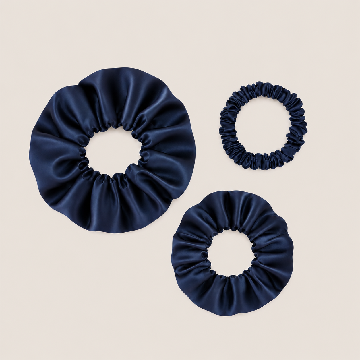 Marineblauwe scrunchies van moerbeizijde in drie maten op een neutrale achtergrond.