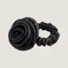 Zwarte scrunchie van moerbeizijde met een sculpturaal rozendetail op een neutrale achtergrond