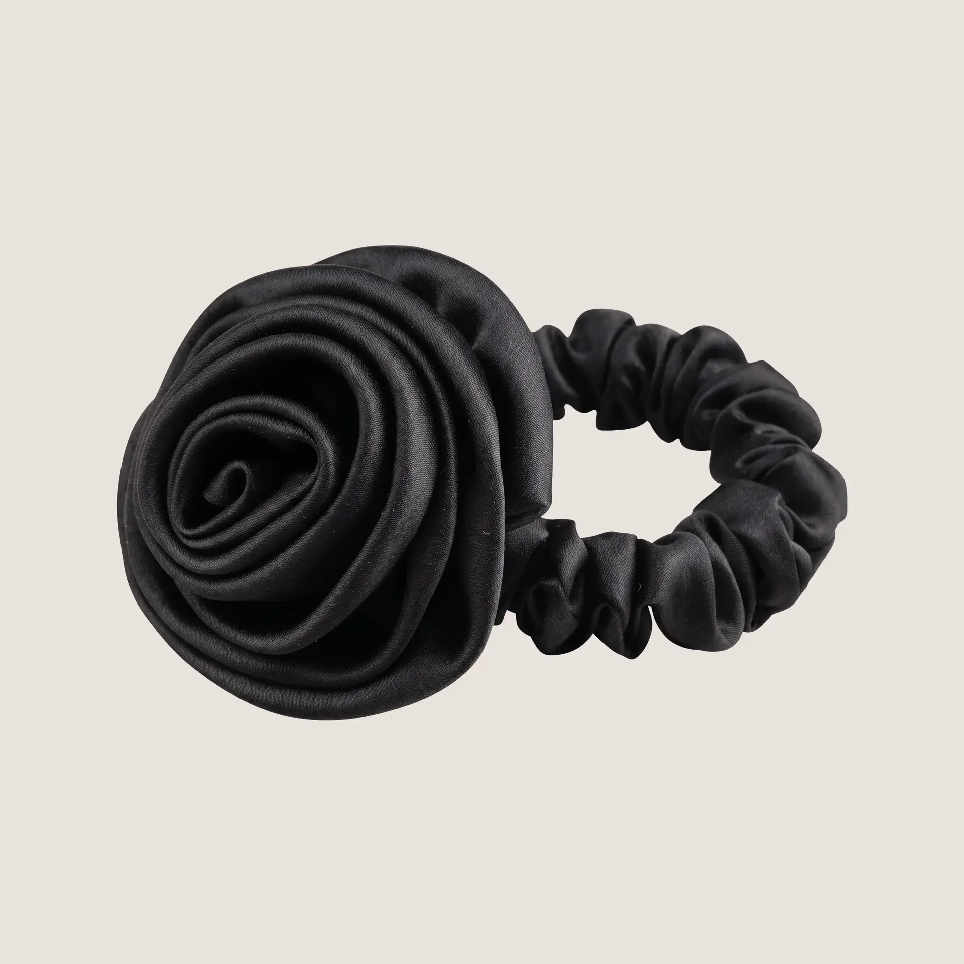 Zwarte scrunchie van moerbeizijde met een sculpturaal rozendetail op een neutrale achtergrond