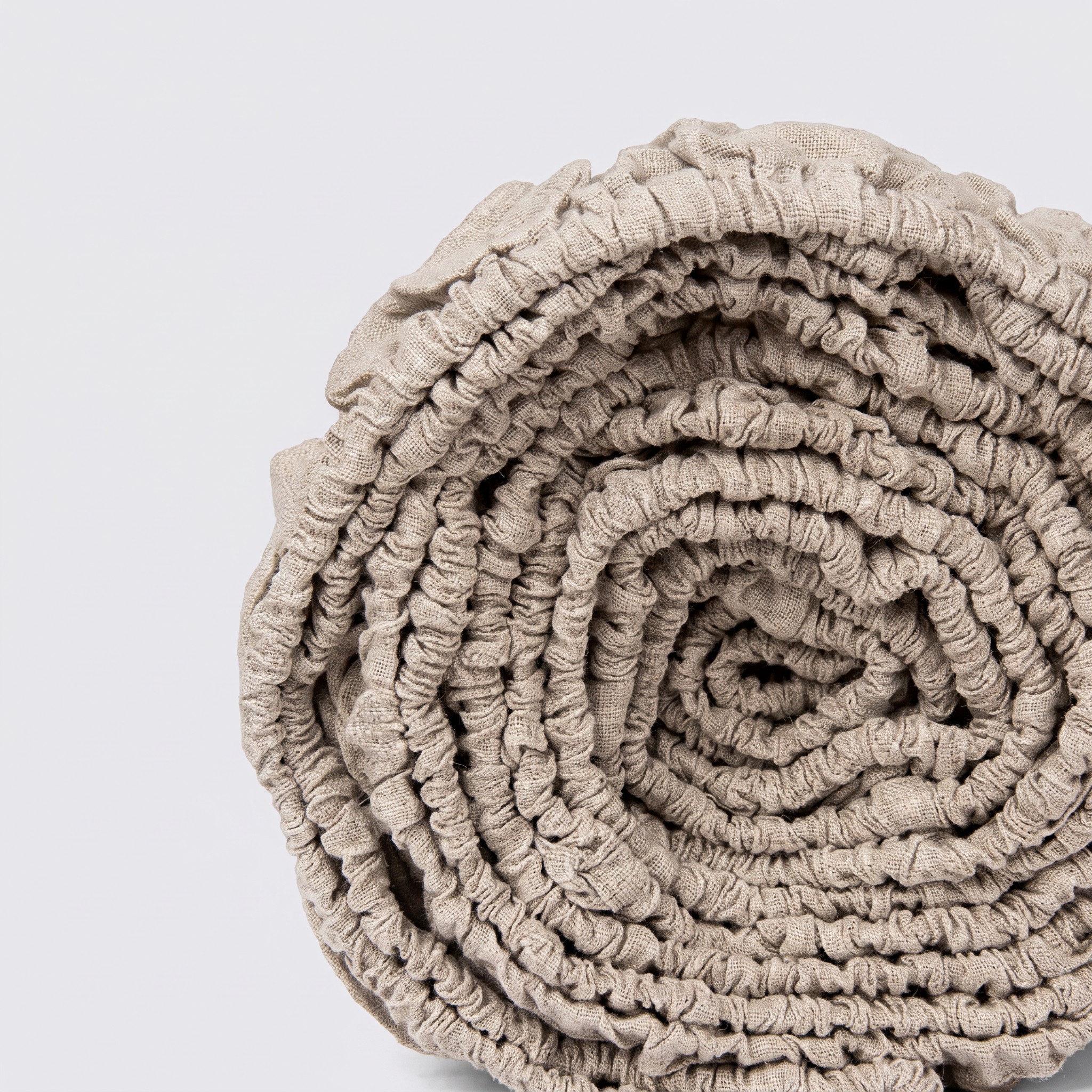 Zusammengerolltes Spannbettlaken aus naturfarbenem Leinen, dessen elastischer Rand sichtbar ist.