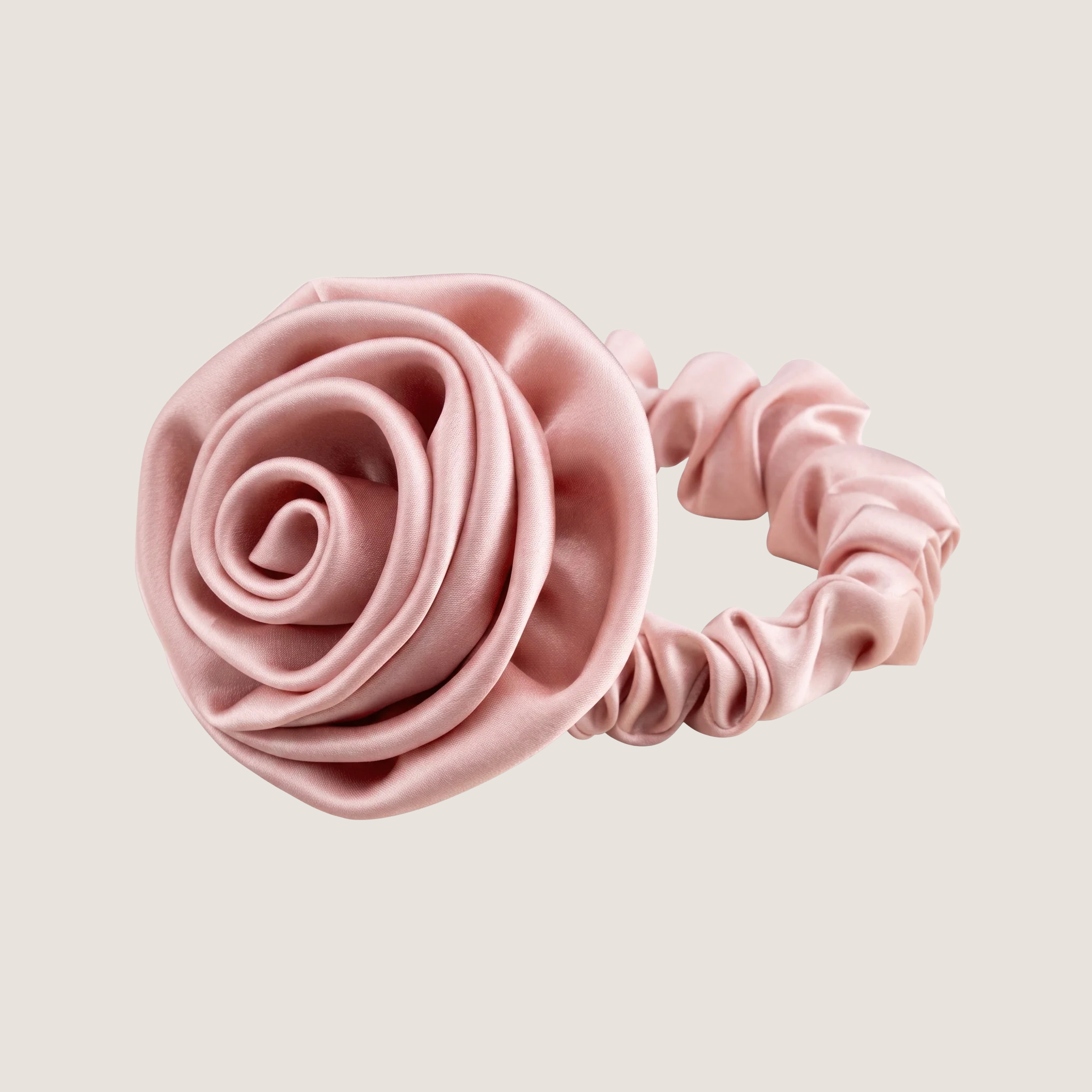 Roze scrunchie van moerbeizijde met een gevormd rozendetail op een neutrale achtergrond.
