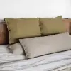 Fundas de cojín Sensoire de lino francés oliva con un cojín cilíndrico de lino natural sobre una cama hecha