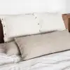 Fundas de cojín Sensoire de lino francés a raya oliva con un cojín cilíndrico natural junto a un cabecero de madera