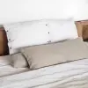 Fundas de cojín Sensoire de lino francés blanco con un cojín cilíndrico de lino natural junto a un cabecero de madera