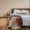 Hellgraue Leinenbettwäsche mit mehreren Lagen Überwürfen in einem warmen Schlafzimmer
