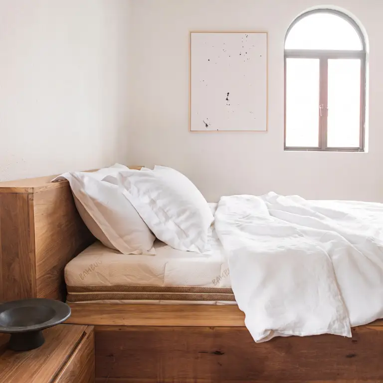 Weiße Leinenbettwäsche und Kissen auf einem hölzernen Plattformbett