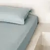 Bettwäsche aus taubenblauem gewaschenem Leinen in einem ruhigen Schlafzimmer