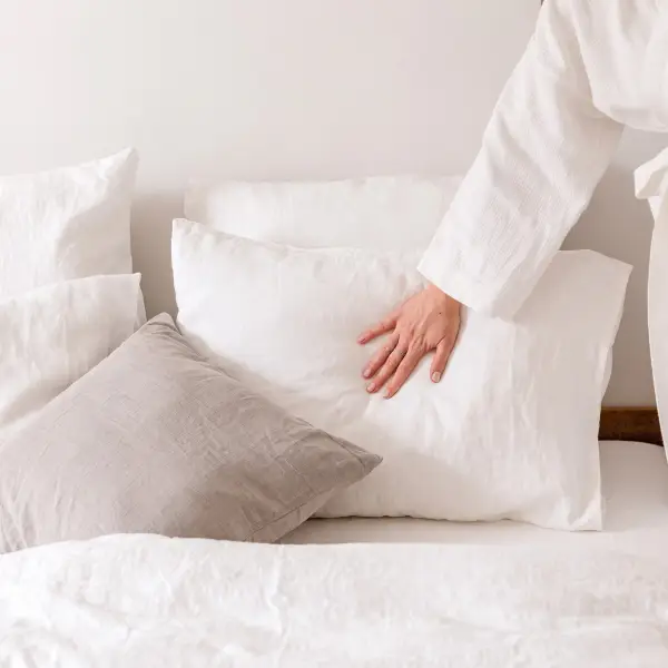Una mano presiona una funda de almohada de lino blanco para mostrar la suavidad y la textura naturales del lino lavado.