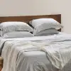 Manta de lino francés marfil con bordes deshilachados a los pies de una cama de lino Sensoire