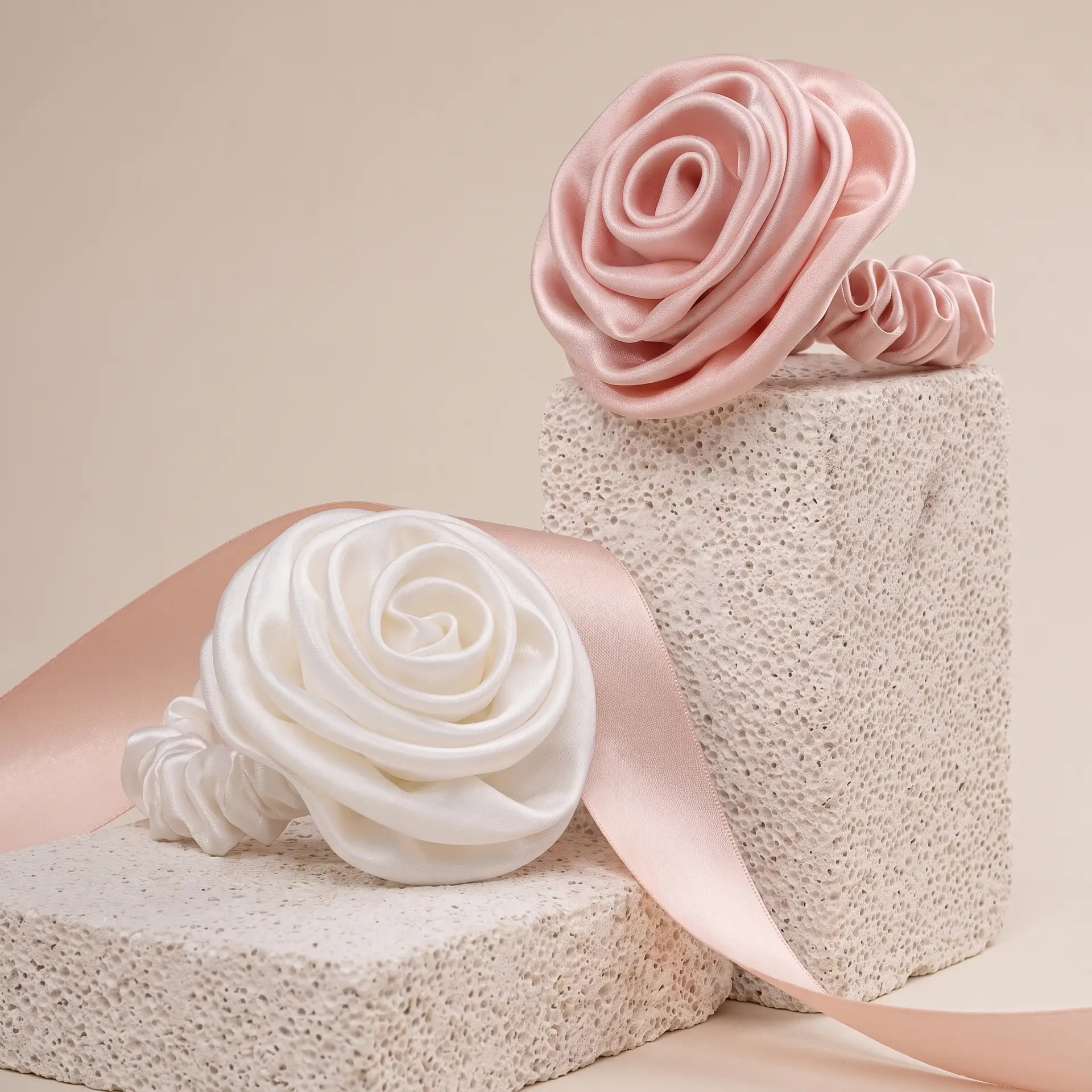 Zijden scrunchies in de vorm van rozen, in zachtroze en ivoor, rustend op een zijden band.