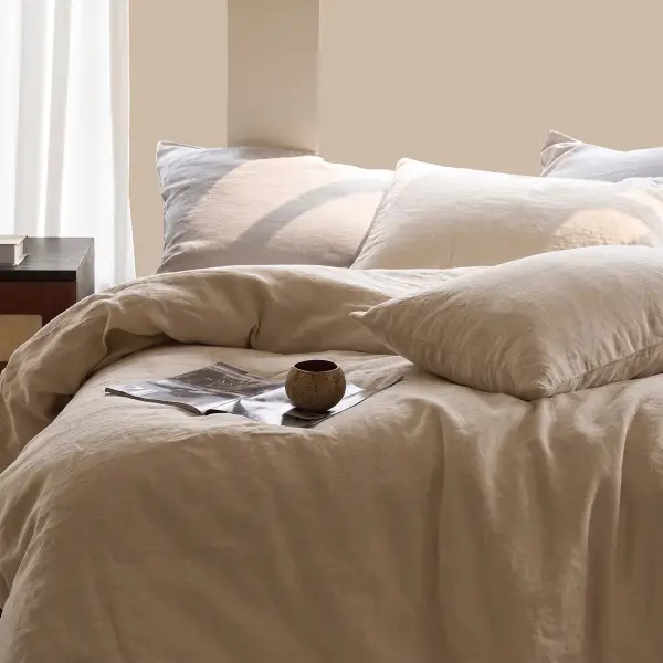 Juego de cama de lino beige natural sobre una cama, con una revista abierta y un pequeño cuenco de madera