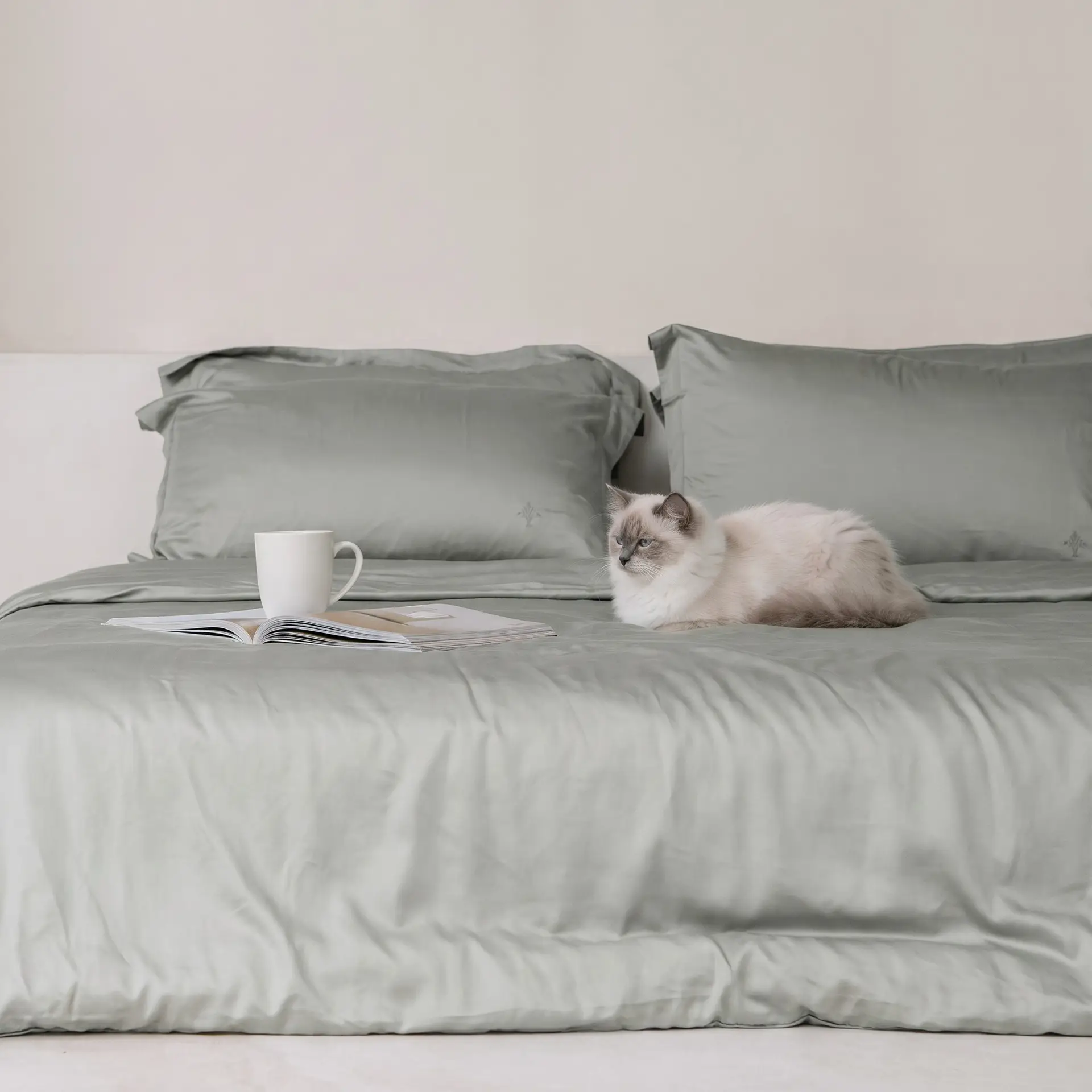 Sensoire Bettbezug aus salbeigrünem Bambus-Lyocell auf einem Bett mit ruhender Katze, aufgeschlagener Zeitschrift und Becher