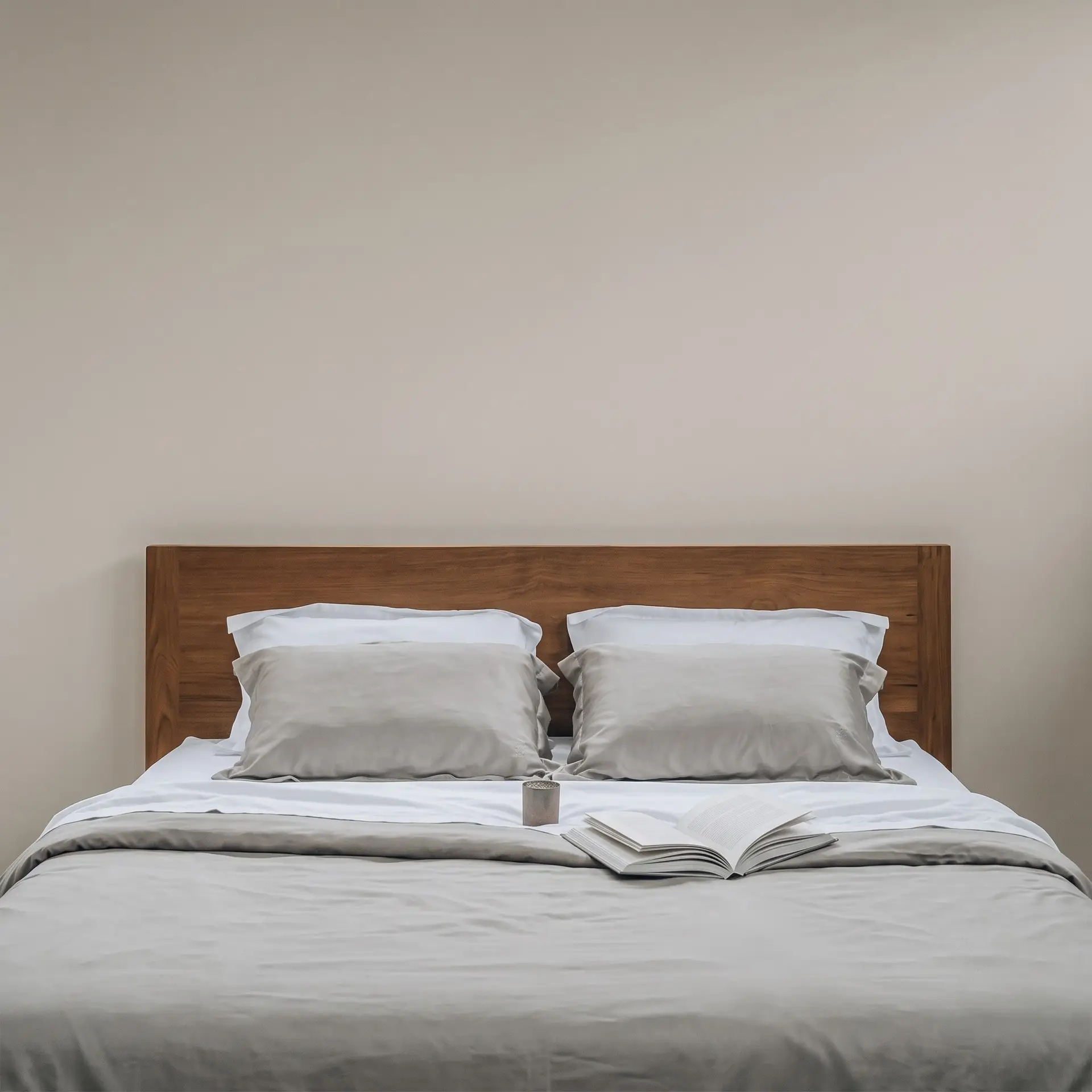 Graue Bettwäsche aus Bambus-Lyocell auf einem Bett mit Holzkopfteil, Buch und Kerze in einem neutralen Schlafzimmer