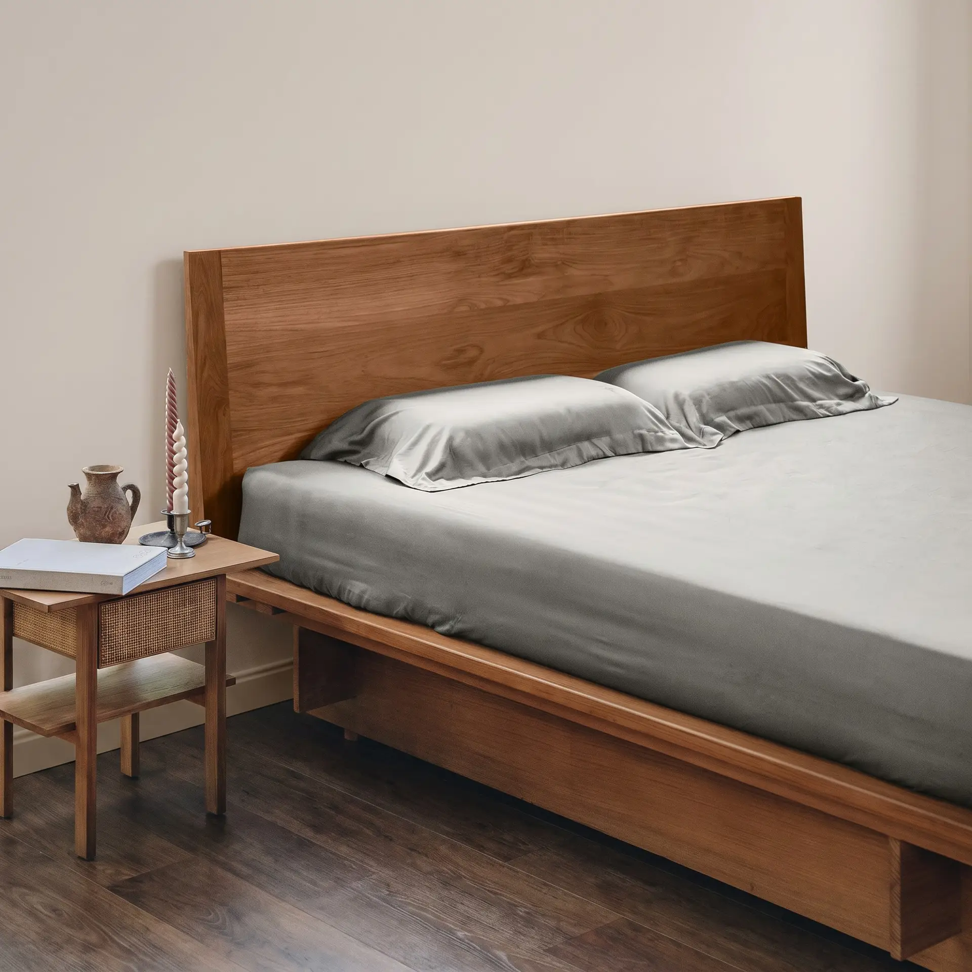 Bettwäsche aus salbeigrünem Bambus-Lyocell auf einem Bett mit hölzernem Kopfteil und einem Nachttisch mit Kerzen.