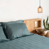 Schieferblaue Kissenbezüge aus Bambus-Lyocell auf einem Bett neben einem Nachttisch in einem neutralen Schlafzimmer