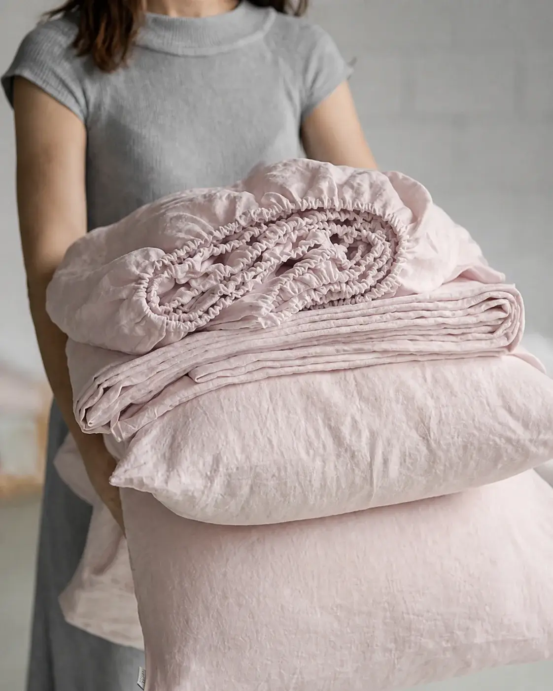 Persona llevando una pila de ropa de cama de lino lavado en rosa empolvado