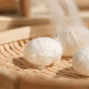 Cocons blancs de soie de mûrier posés sur un plateau en bambou tressé