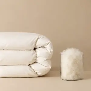Une couette blanche pliée à côté d'un bocal en verre rempli de flocons de duvet