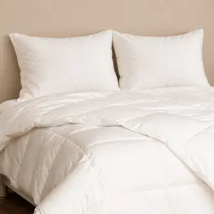 Une couette blanche piquée et bien gonflée sur un lit avec deux oreillers blancs
