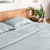 Sensoire-Bettwäsche aus himmelblauem Bambus-Lyocell auf einem Bett neben einem hölzernen Nachttisch und grünen Pflanzen.