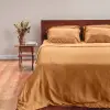 Senffarbener Sensoire Bettbezug aus Bambus-Lyocell auf einem Bett mit Holzkopfteil, daneben Trockenblumen