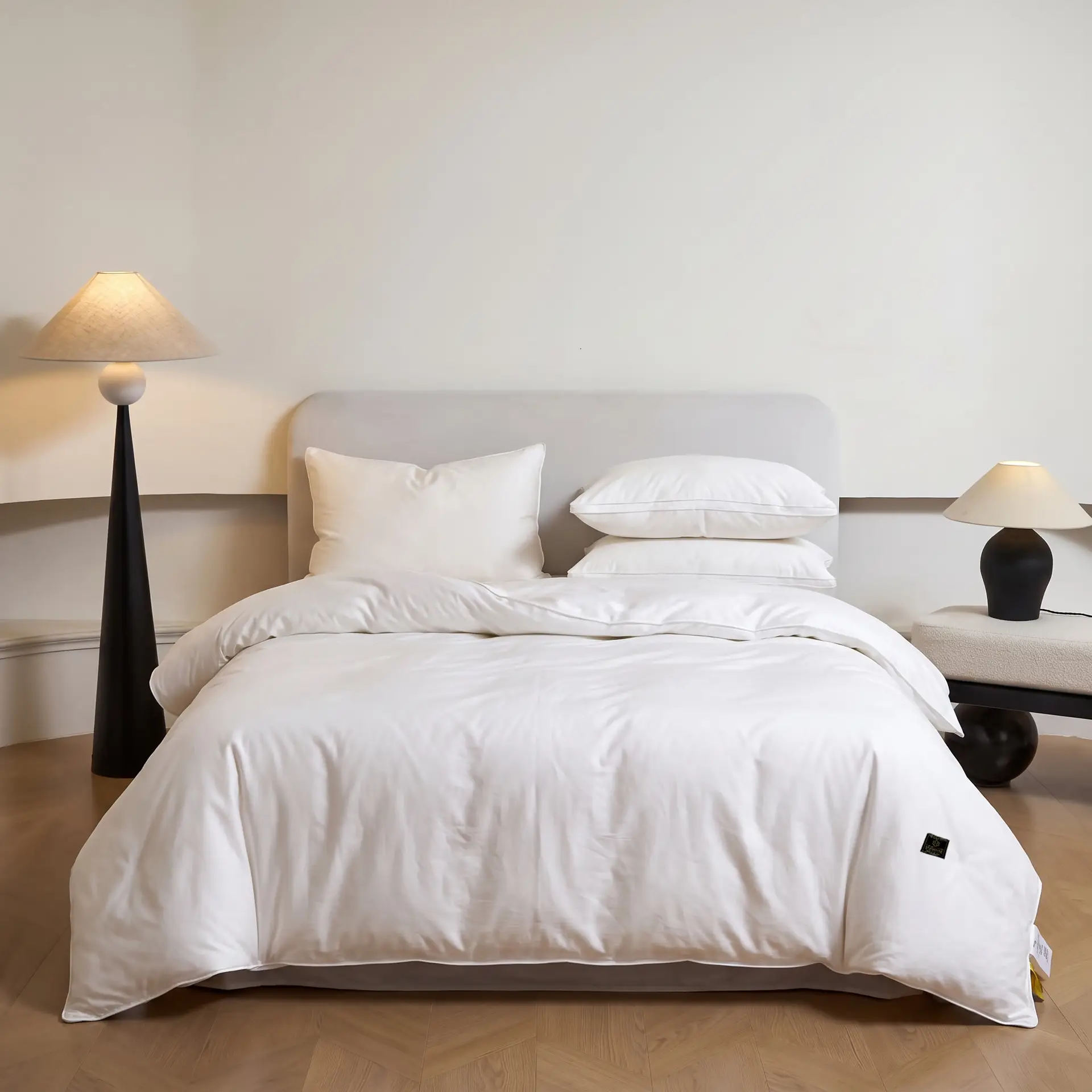 Schlichte elfenbeinfarbene Bettdecke auf einem sanft beleuchteten Bett in einem warm-neutralen Schlafzimmer.
