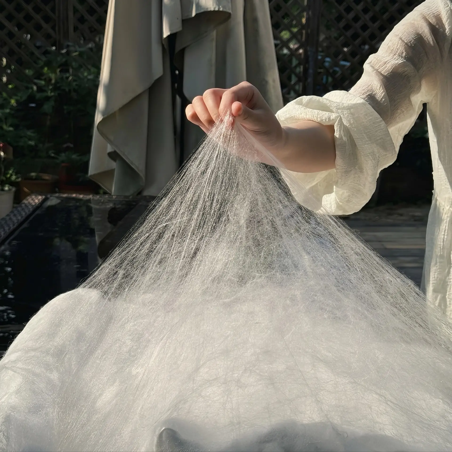 Une main soulevant une nappe vaporeuse de soie floche à longs fils vers la lumière
