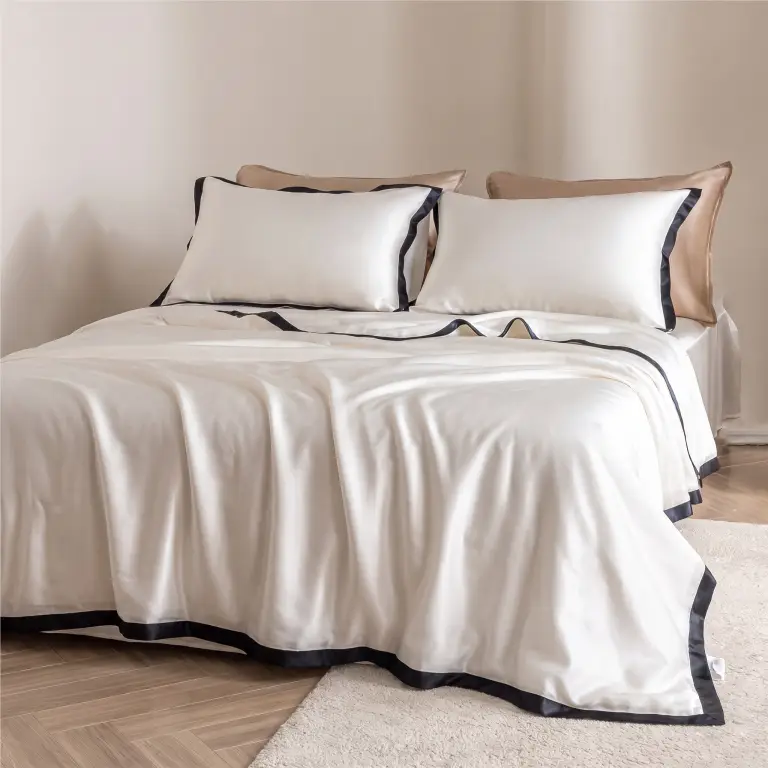 Noir Contour Bettwäsche-Set aus weißer Seide mit schwarzer Bordüre in einem sanft beleuchteten Schlafzimmer in Naturtönen