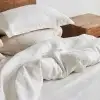Weiße Kopfkissenbezüge und Bettbezug aus Hanf auf einem ungemachten Bett