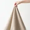 Eine Hand hebt Hanfstoff in Natur an und zeigt seinen weichen Fall
