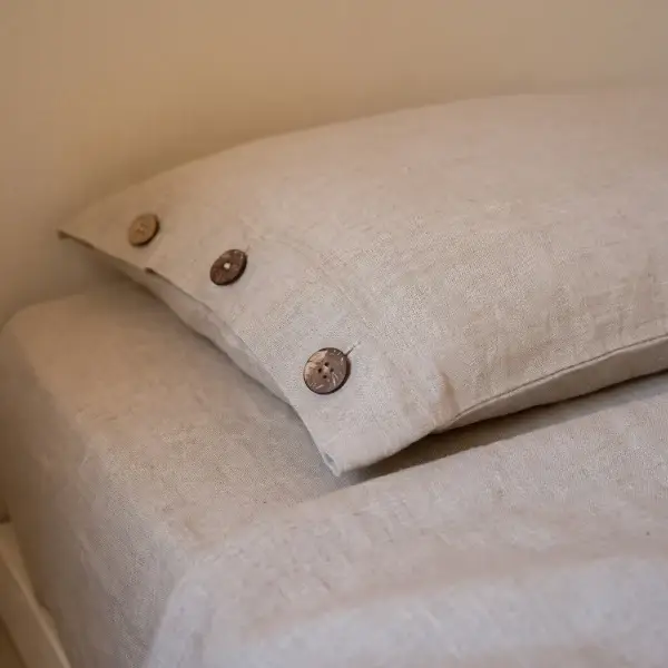 Kopfkissenbezug aus Hanf in Natur mit drei Kokosnussknöpfen auf einem Bett