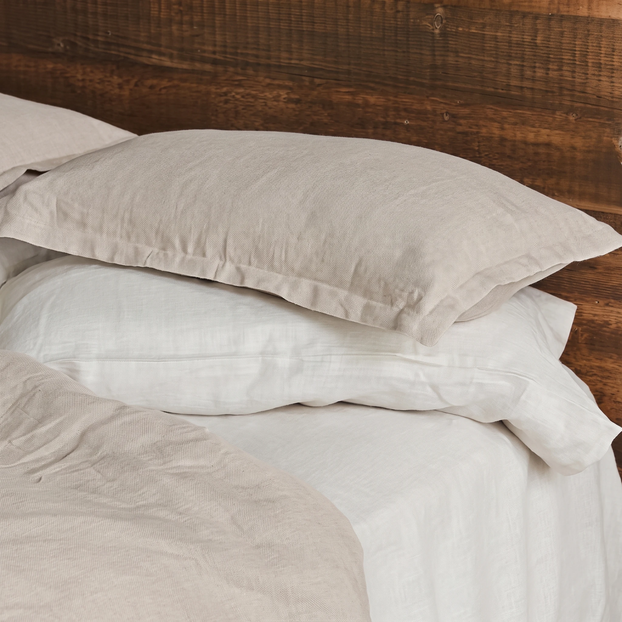 Kopfkissenbezüge aus Hanf mit Hotelverschluss in Natur und Weiß auf einem Holzbett