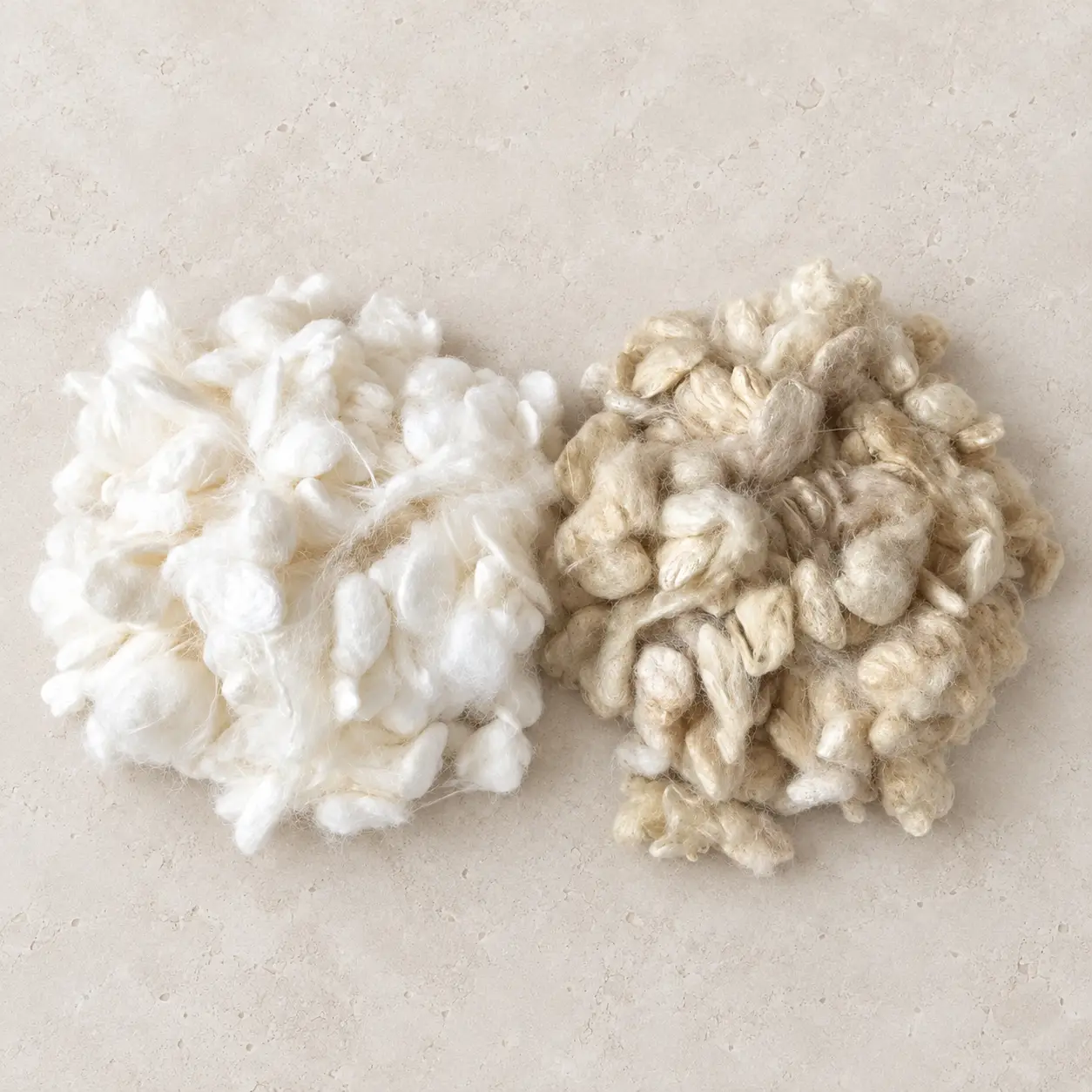 Cocons de soie blancs et fauves disposés côte à côte sur une surface de pierre claire.