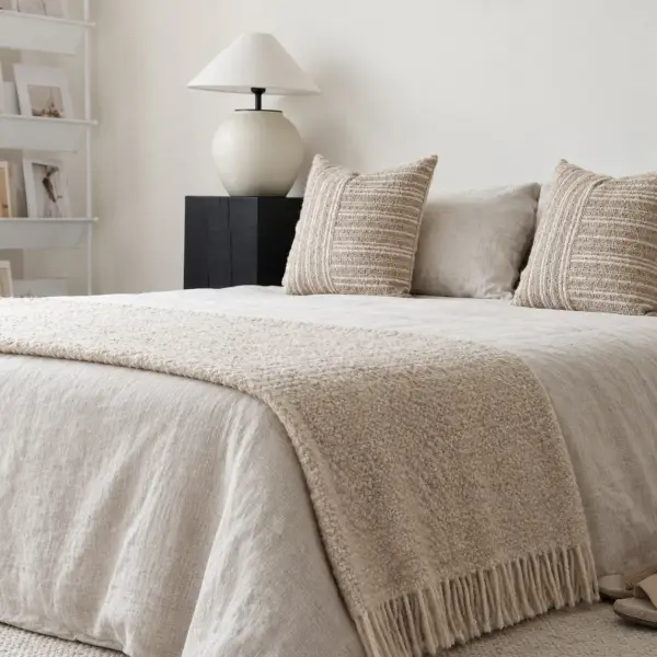 Una manta de lino natural con flecos a los pies de una cama vestida con lino blanco