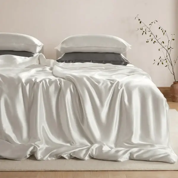 Ivoorkleurig dekbedovertrek van moerbeizijde op een bed, met ivoorkleurige en grijze zijden kussenslopen