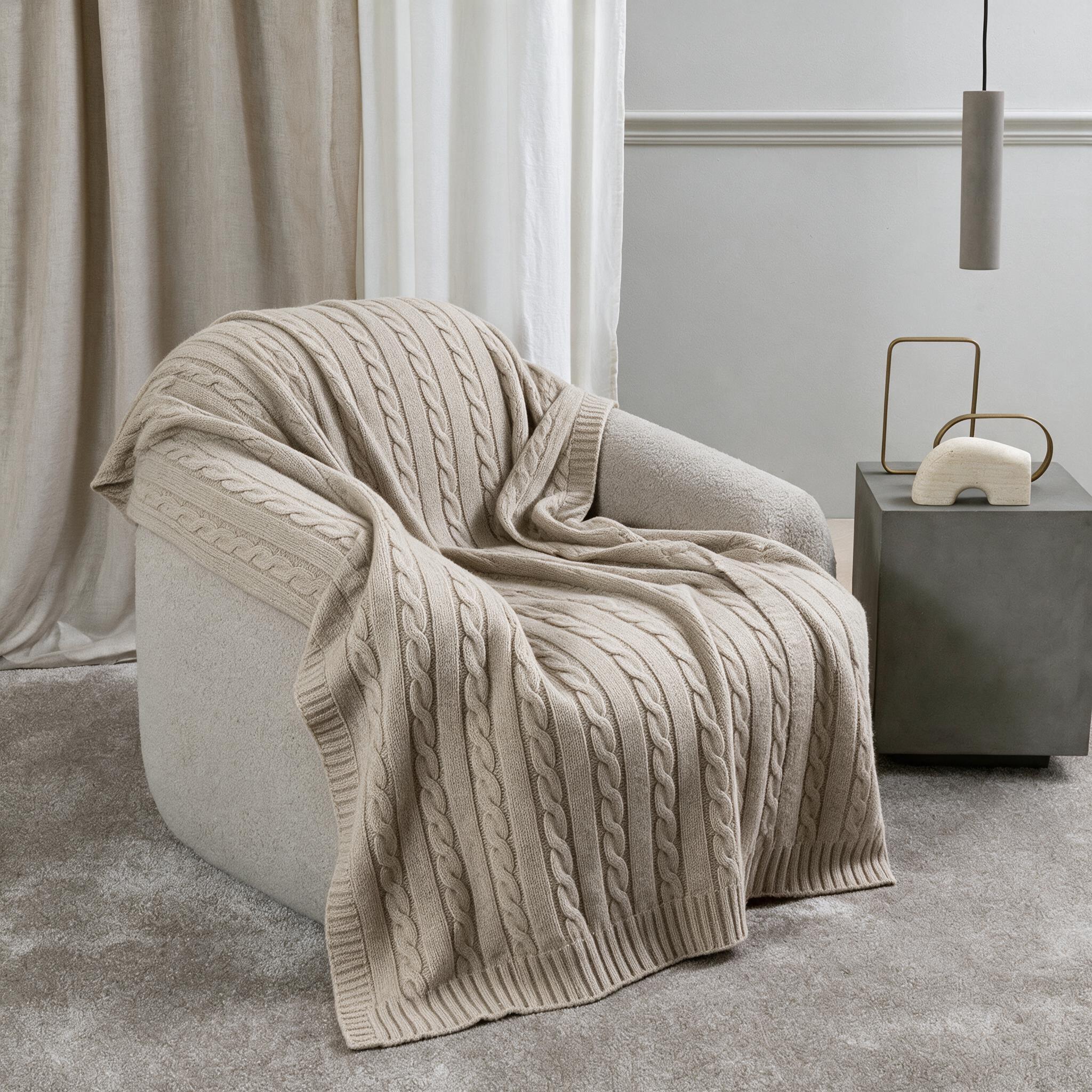 Manta de cashmere avena con punto de ochos sobre un sillón blanco mullido