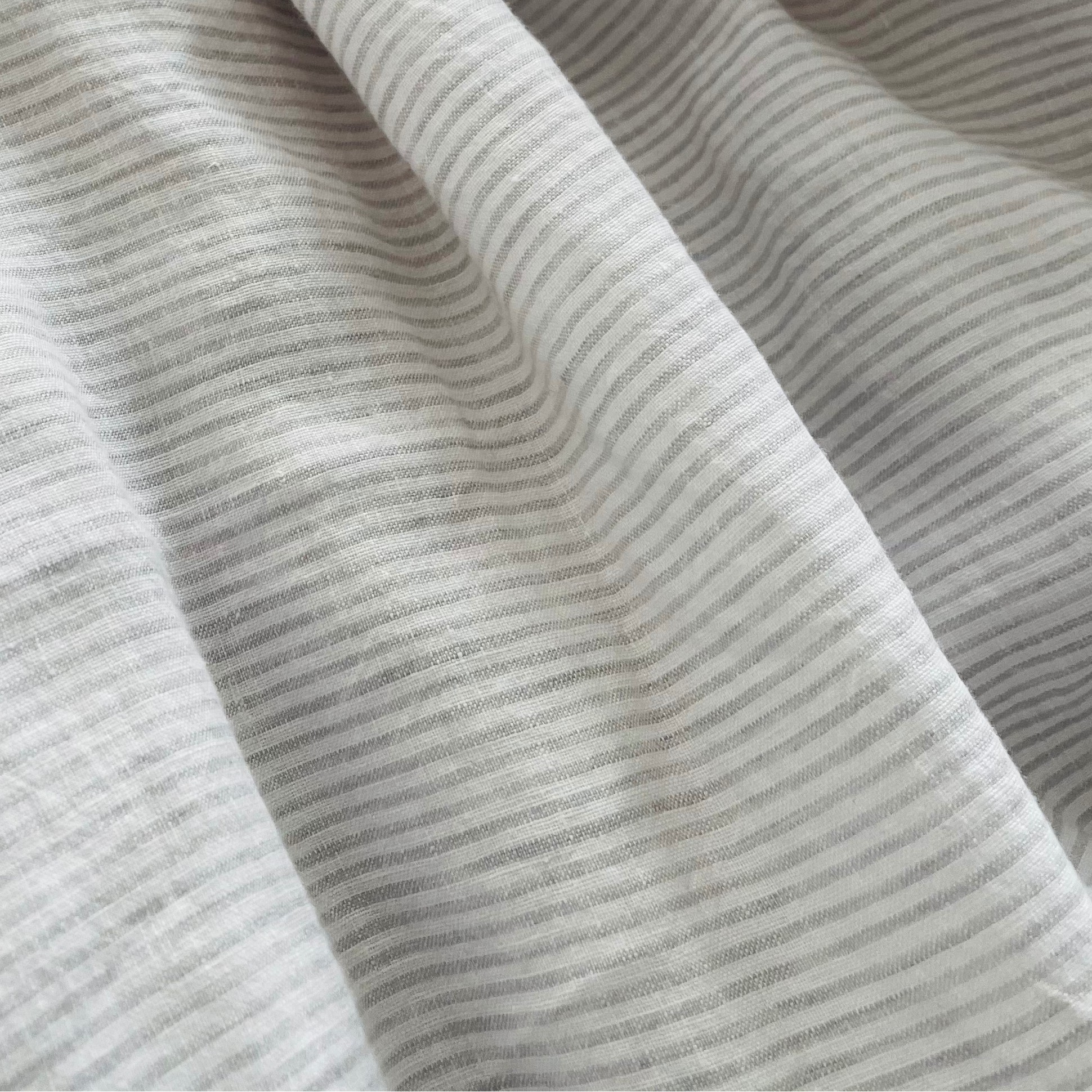 Gros plan sur un lin tissé de fines rayures régulières blanches et gris doux