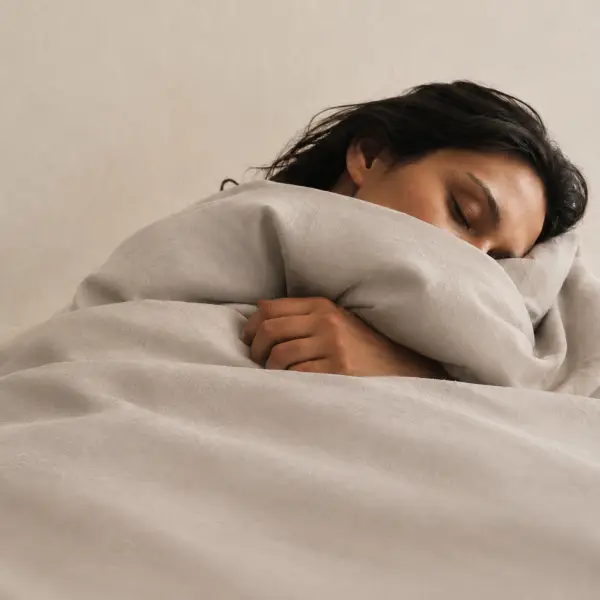 Een slapende vrouw, tot aan haar kin toegedekt met zacht grijs beddengoed