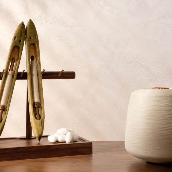 Twee houten weefspoelen, zijdecocons en een klos ivoorkleurig zijdegaren op een notenhouten tafel