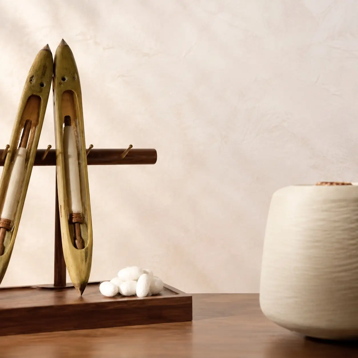Due navette da tessitura in legno, bozzoli di seta e un cono di filo di seta avorio su un tavolo in noce