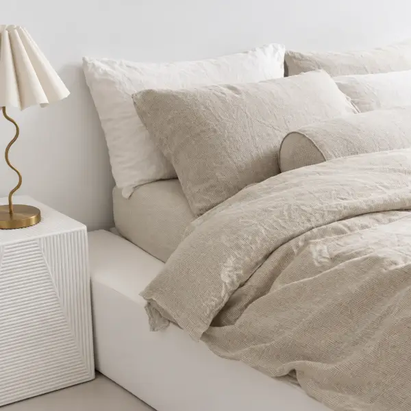 Ungemachtes Bett mit naturfarbenem Leinen und weichen Falten, daneben ein weißer Beistelltisch und eine Messinglampe