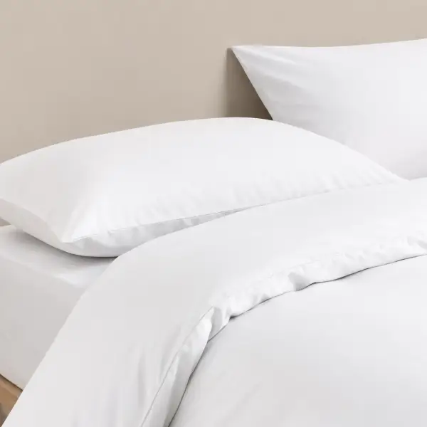 Witte kussenslopen en dekbedovertrek van lyocell op een bed tegen een grijsbeige muur